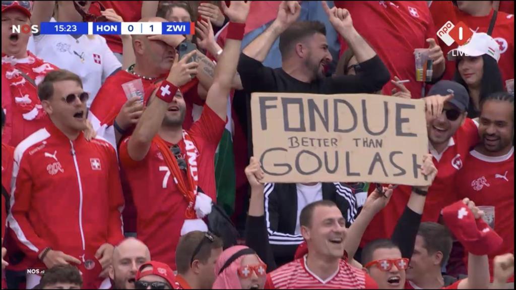 Schweizer Nati-Fans am EM-Spiel Schweiz-Ungarn am 15.06.2024. Einer hält einen Karton hoch mit der Aufschrift «Fondue better than Goulash».
